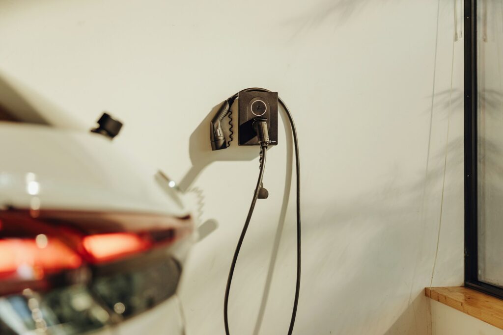 A car parked at a wall-mounted home charge point on a new-build driveway.