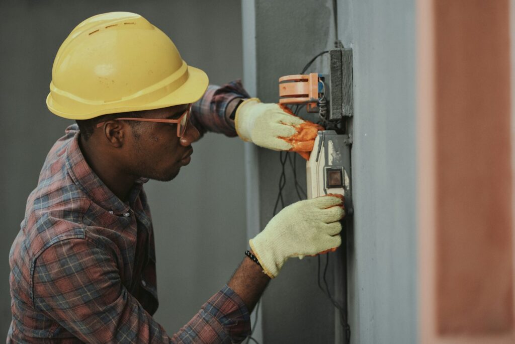 An electrician in a hard hat working on an exterior meter enclosure.