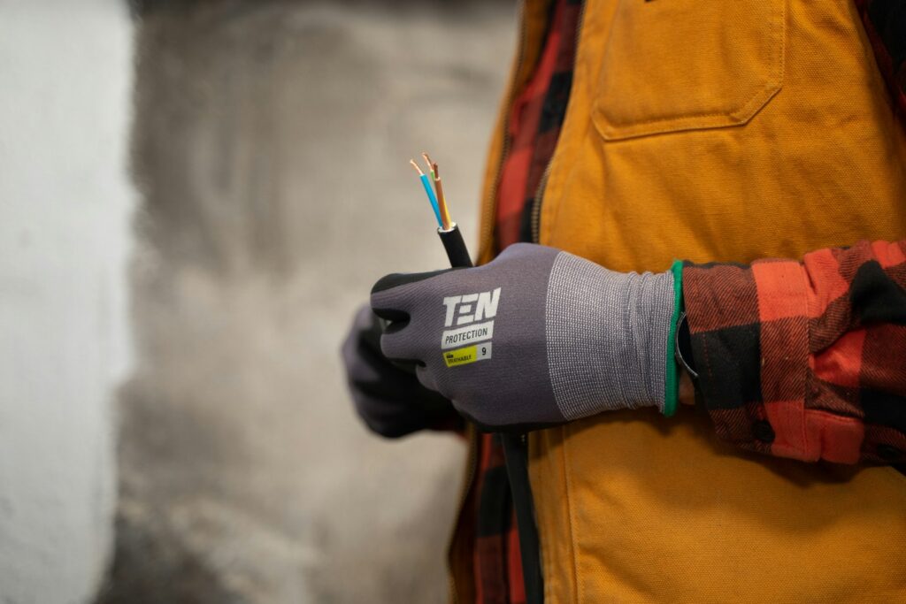 A gloved hand holding stripped cable cores against a bare plastered wall during a first fix.