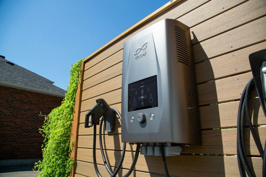 A home electric vehicle charge point mounted on a timber-clad house wall, cable coiled beneath it.